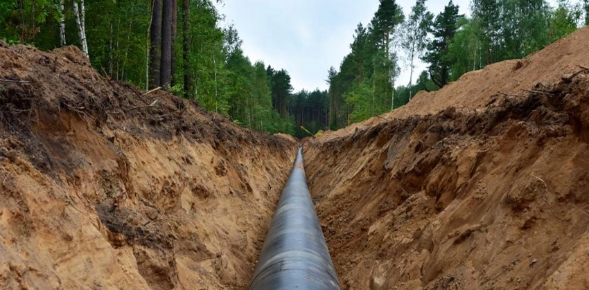 A large pipe is being built in a trench in the woods.