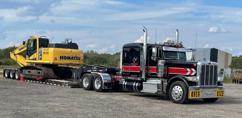 HOMATS semi truck transporting a Komatsu excavator on a flatbed trailer.
